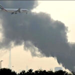 An Emirates aircraft flies past plumes of smoke from a fire caused by an Iranian drone attack near Dubai International Airport, Dubai, UAE