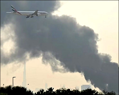An Emirates aircraft flies past plumes of smoke from a fire caused by an Iranian drone attack near Dubai International Airport, Dubai, UAE